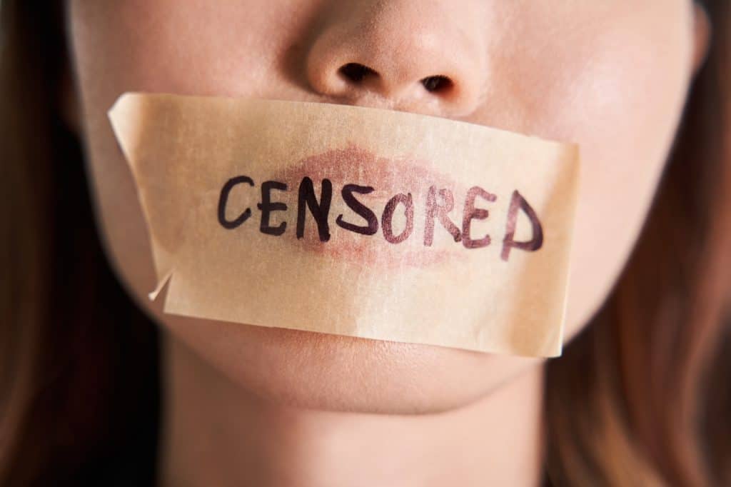 Close up photo of bottom half of woman's face with tape over her mouth, the word 'censored' is written on the tape in capital letters.