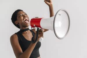 Short-haired Black woman shouting passionately into a megaphone with her arm raised.