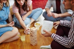 Group sat together on the floor playing game with wooden building blocks, one of girls taking out wooden brick from construction on the floor. Image by freepik.