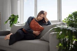 Postnatal depression. A sad young woman sat at home on sofa holding cushion.